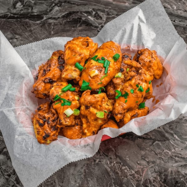 A basket of orange-glazed chicken wings, garnished with chopped green onions, on a dark marble surface.