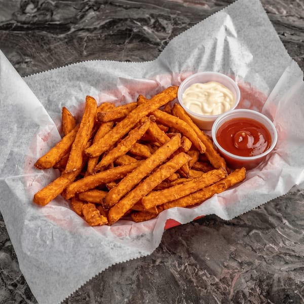 Sweet potato fries in a paper-lined basket with small cups of ketchup and mayonnaise.
