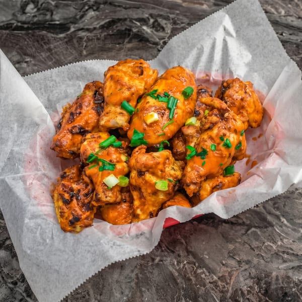A basket of orange-sauced chicken wings topped with green onions, on a dark marble surface.