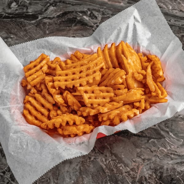 A red basket filled with crispy golden waffle fries, lined with white paper, on a dark marbled surface.