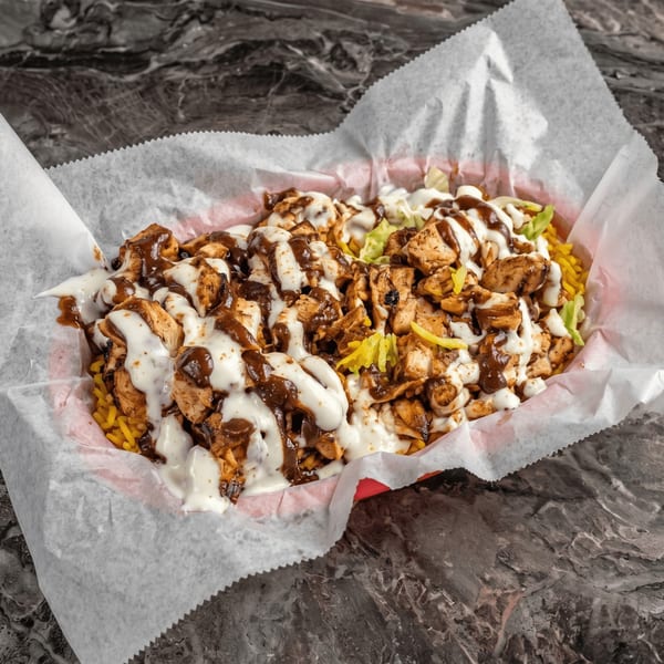 Chicken and rice platter with white and brown sauces, and lettuce, in a red basket with white paper.
